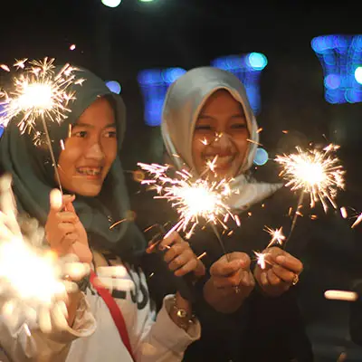 Women wearing traditional head wraps waving sparklers.