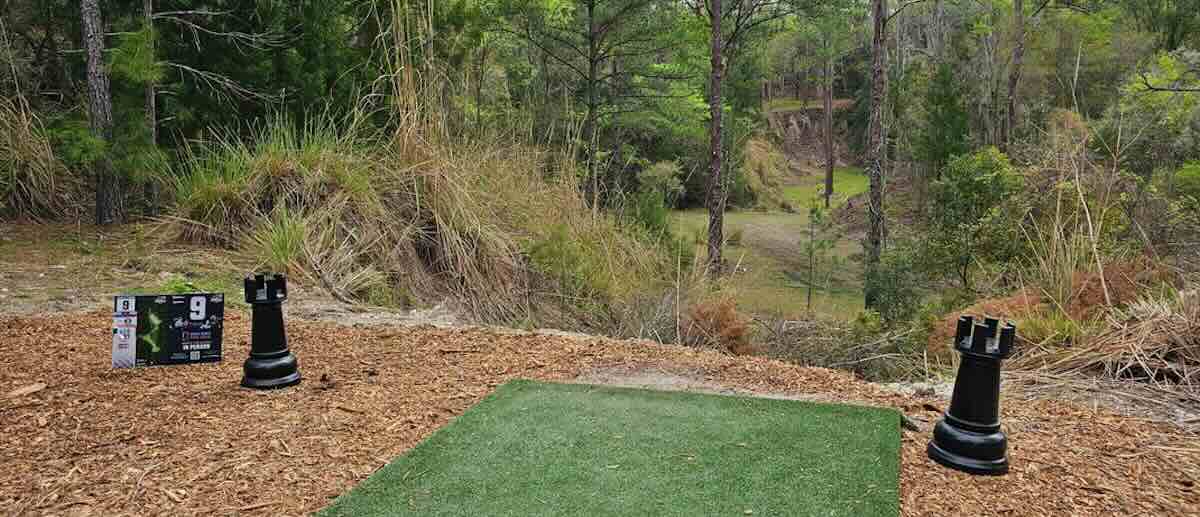 A turf disc golf tee pad near a ledge in a wooded area