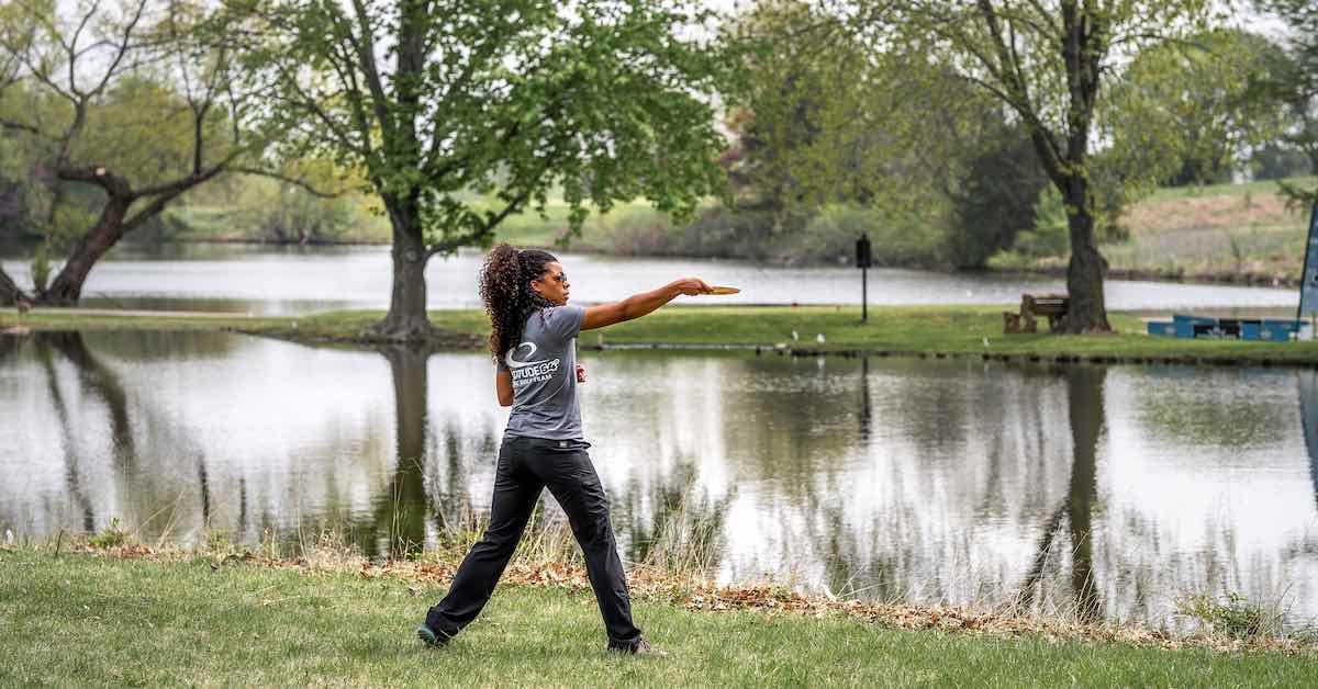 A woman lines up a disc gol shot on well-mown grass near a body of water