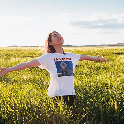 Woman in a field smiling with arms open.