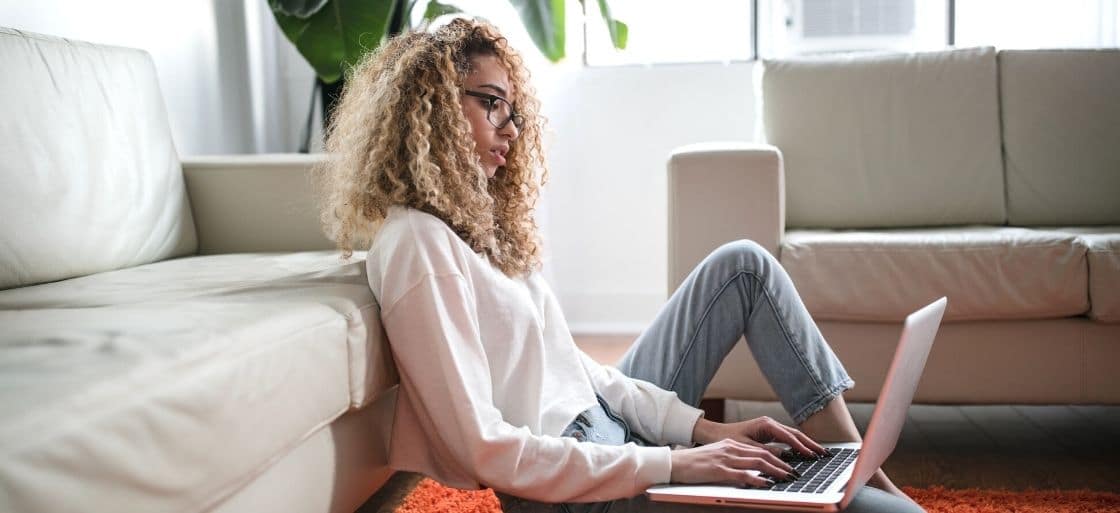 A woman sitting down on the floor, using a laptop.