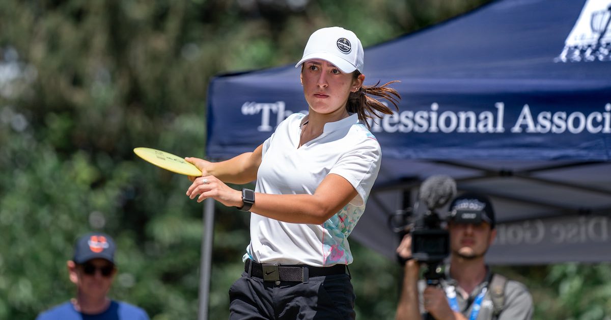 A young woman in a baseball hat prepares to throw a disc golf shot