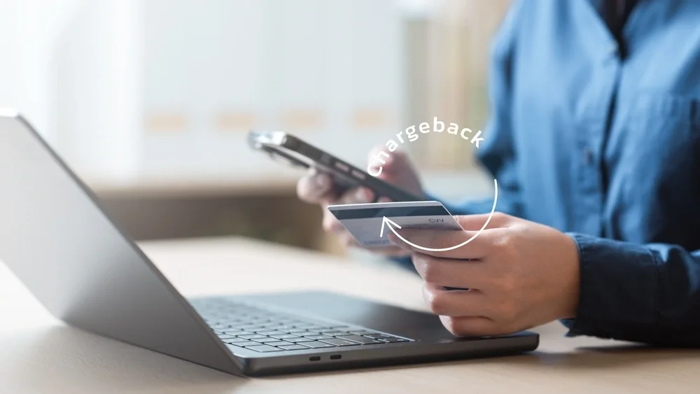 Close up of a man at his laptop holding a credit card in one hand and a mobile phone in the other