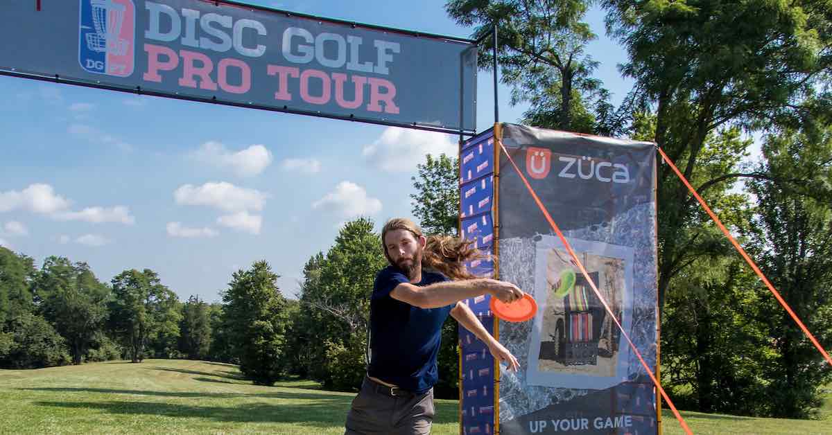 A man reaching back to throw a disc on a bright day under a banner saying Disc Golf Pro Tour above and ZÜCA to his right