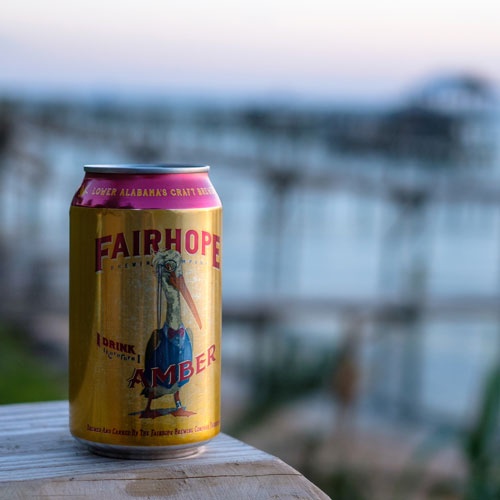 Fairhope Brewery beer sitting on wooden dock with view behind.