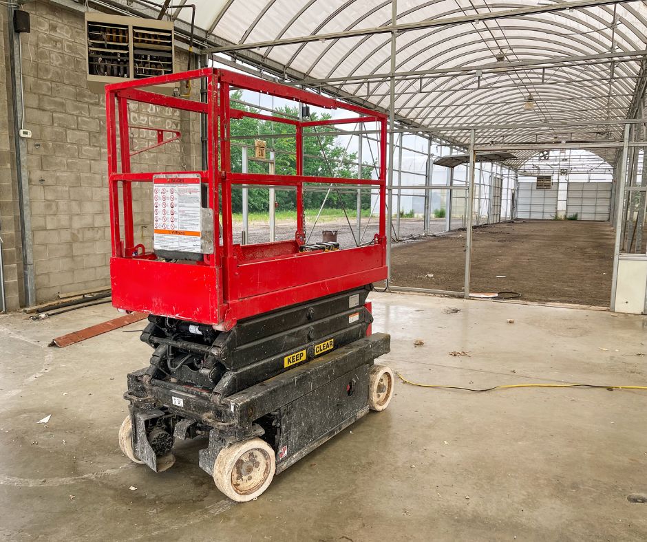 Red scissor lift in a greenhouse construction site