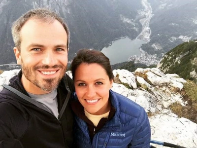 Couple standing on a mountaintop with a lake in the background