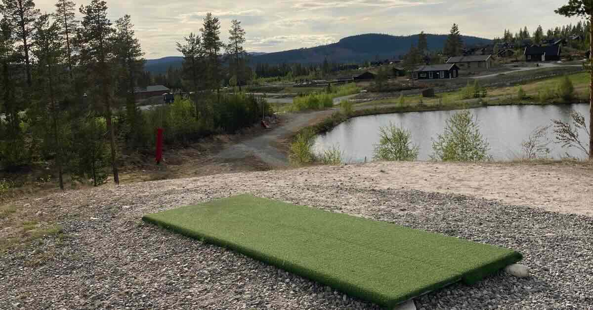 Red disc golf baskets in a field with running water in the foreground