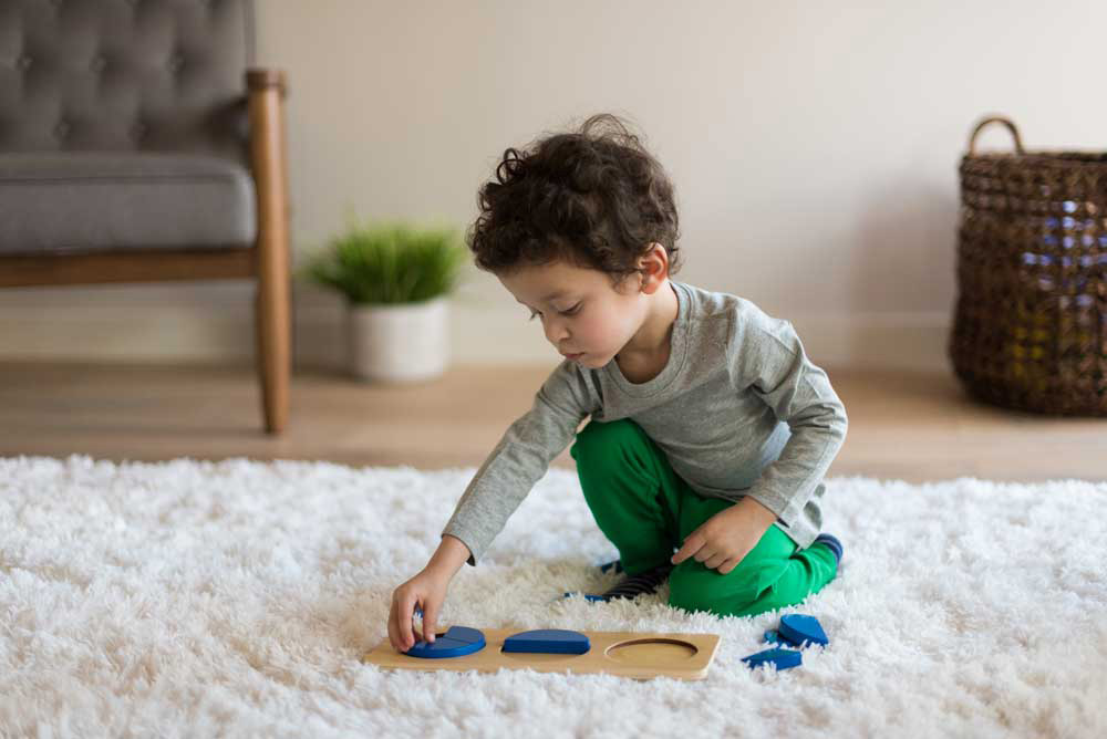 toddler wearing gray and green solving a wooden puzzle