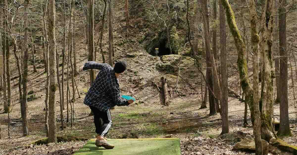 A man throws a disc golf forehand in a wooded area