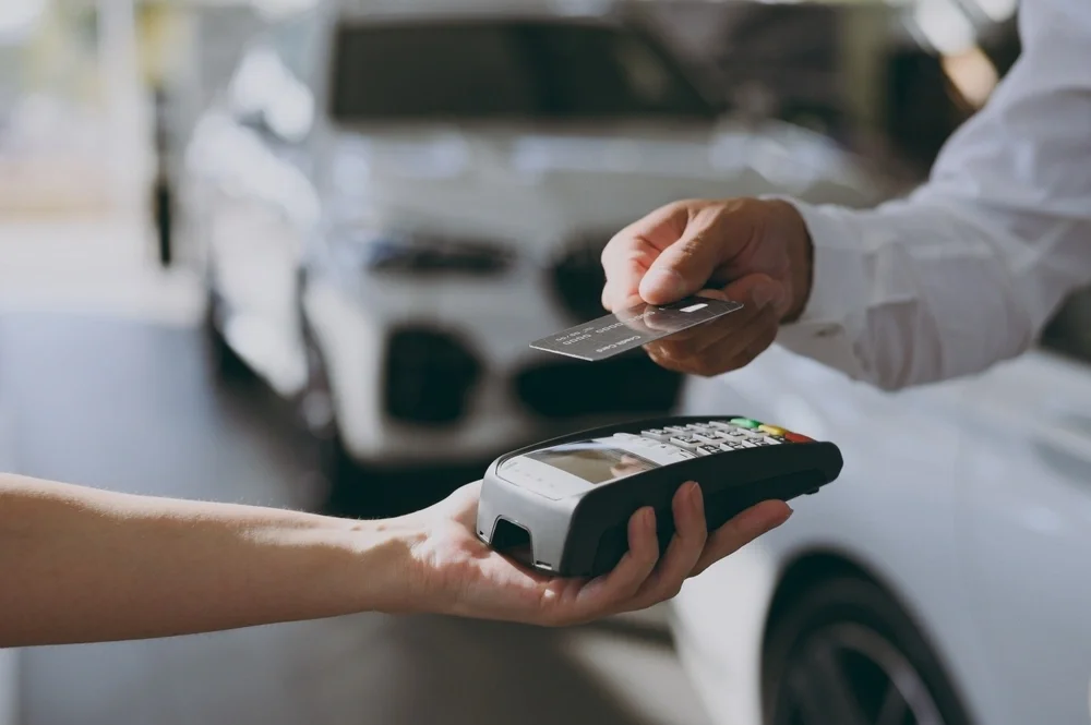 someone paying contactless with their credit card, with a car dealership in the background