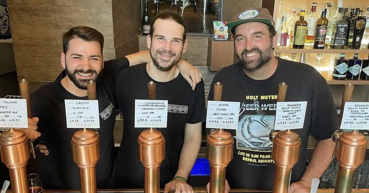 Three men posing for a photo at a bar behind beer taps