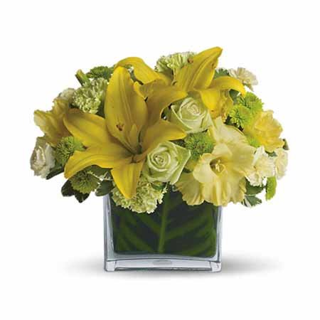 Yellow lily pale green roses inside a leaf lined square vase