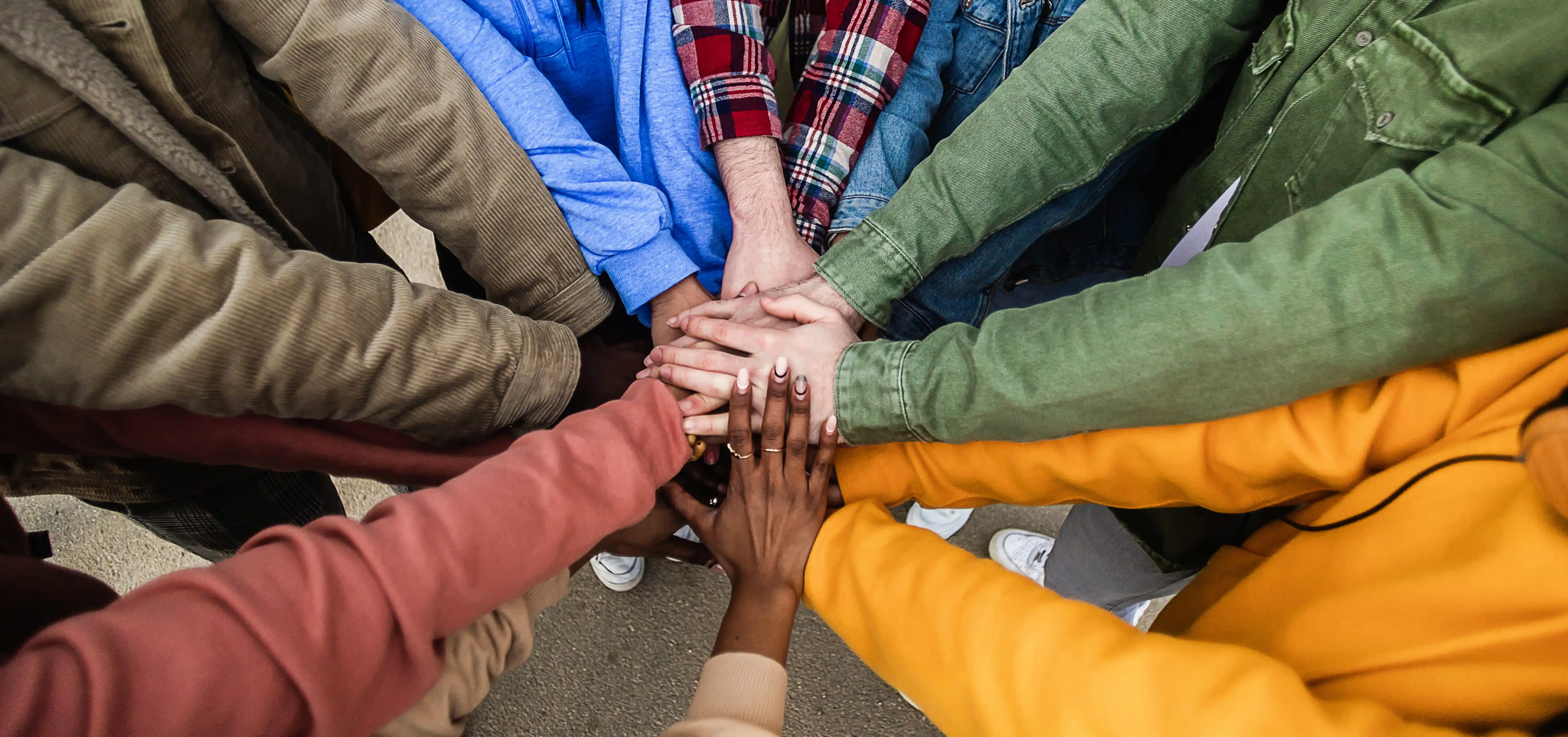 Diverse group stacking hands outdoors representing shared values and cultural unity in global managed teams