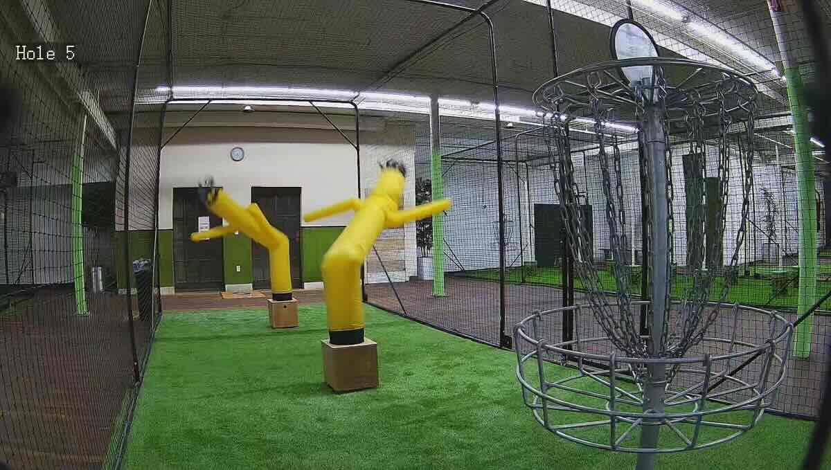 A disc golf basket indoors with waving, air-filled tube men in front of it like defenders