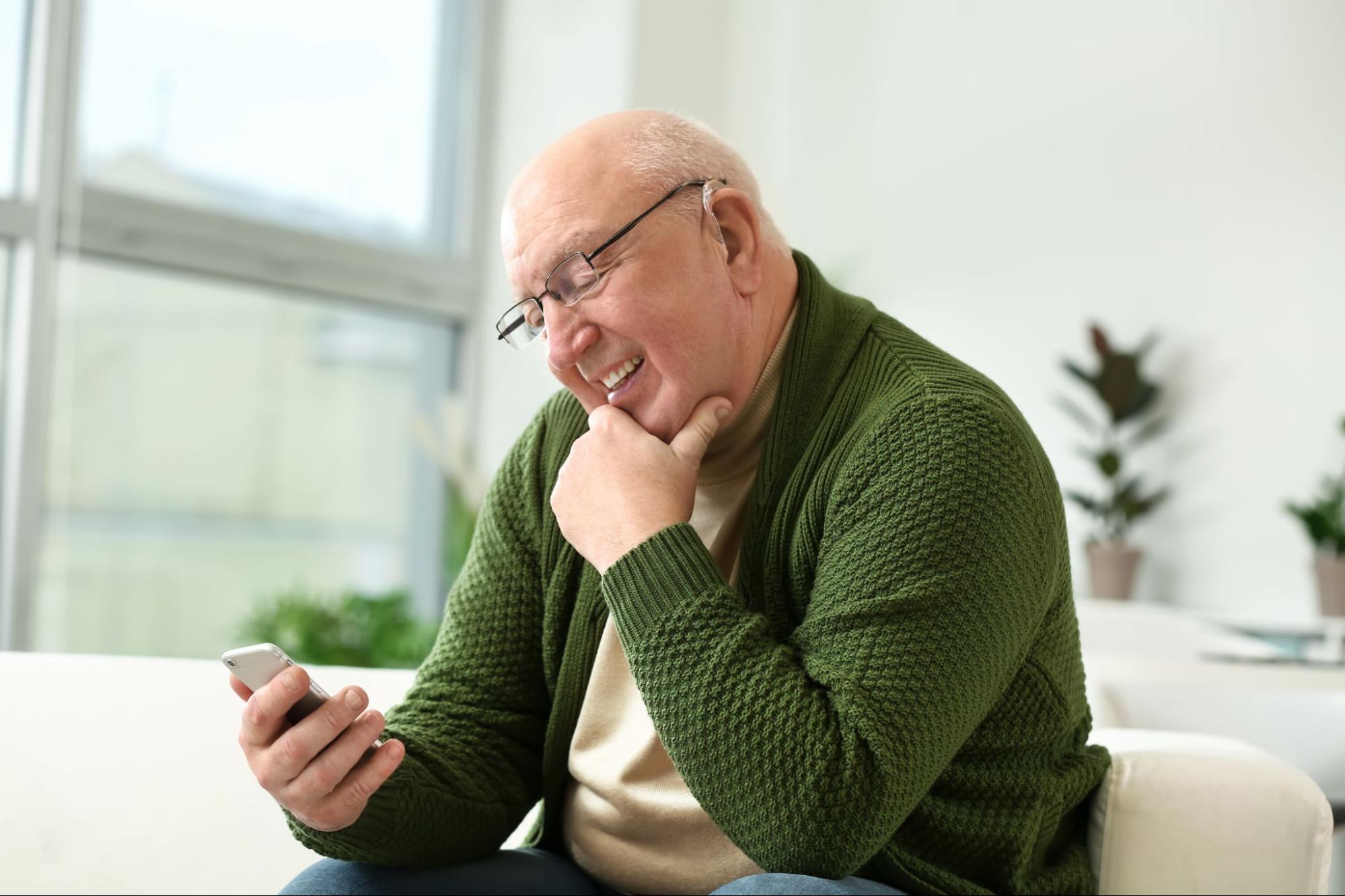 Hearing Care Solutions: old man smiling while looking at his phone