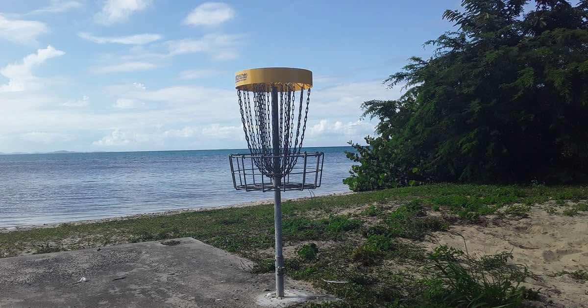 A disc golf basket with a yellow band in front of water