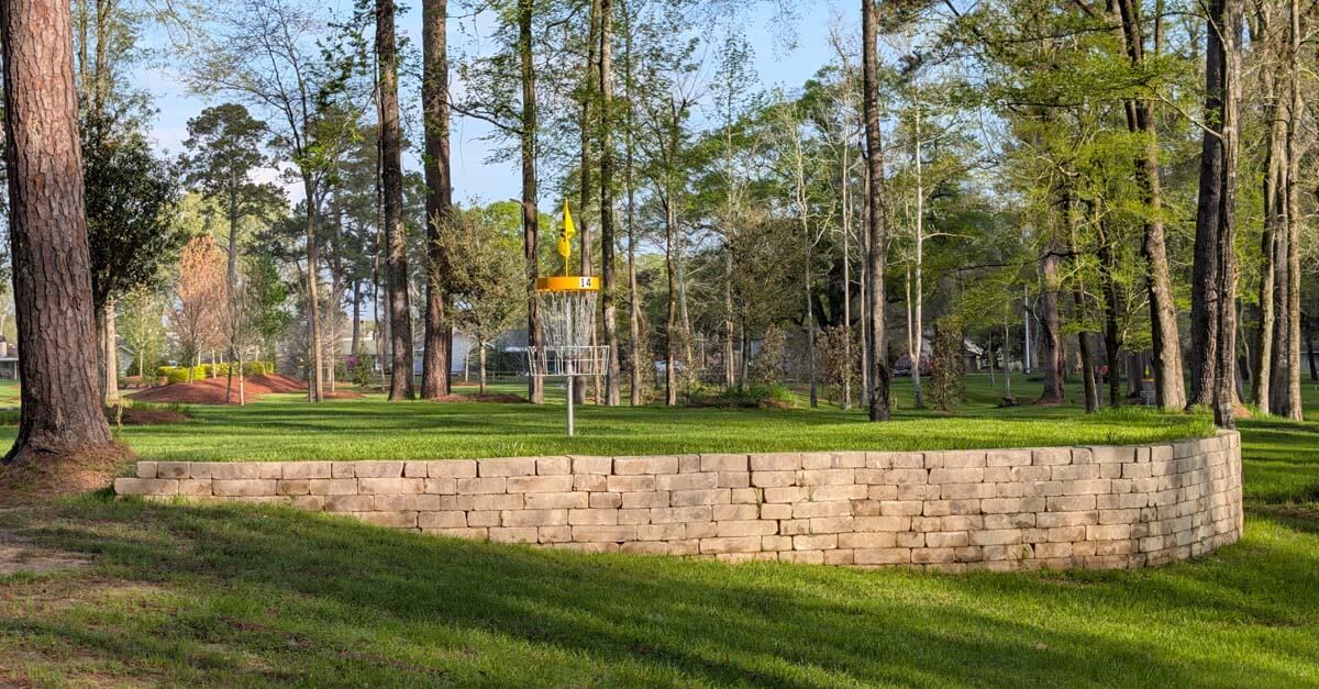 A disc golf basket on an elevated mown area surrounded by a round stone wall