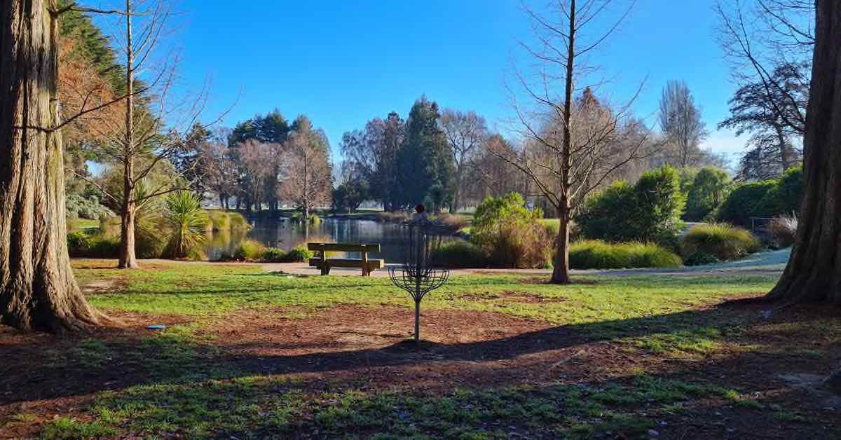 a disc golf basket in a park in front of a small lake