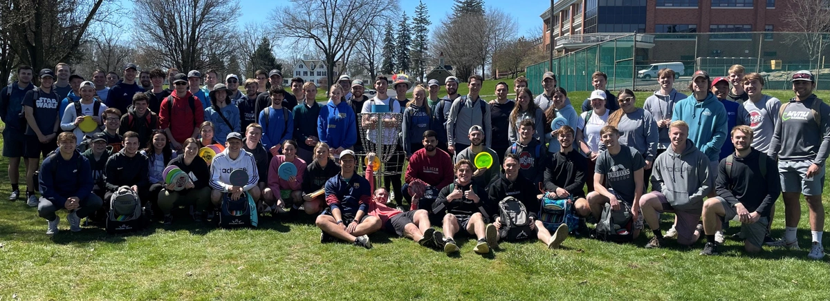 Group of young people with discs smiling in front of a disc golf basket.