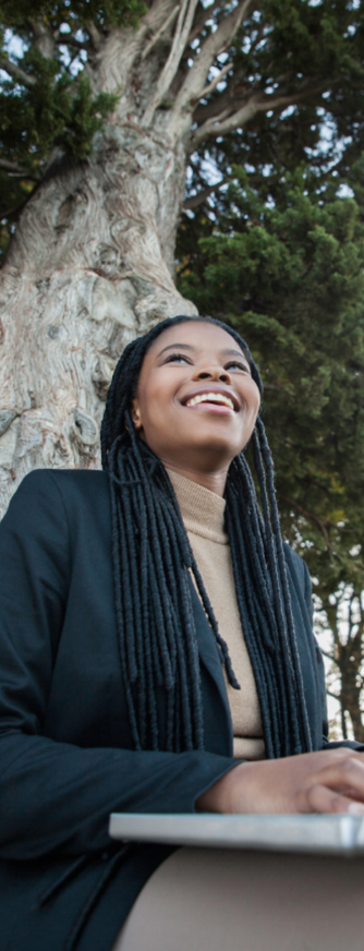 a woman at a laptop, sitting at a tree