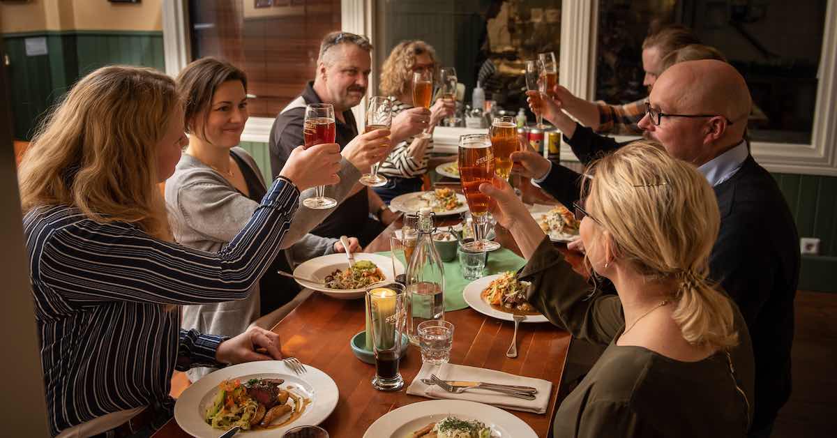 A group of people raise glasses of beer in a toast at a semiformal dinner