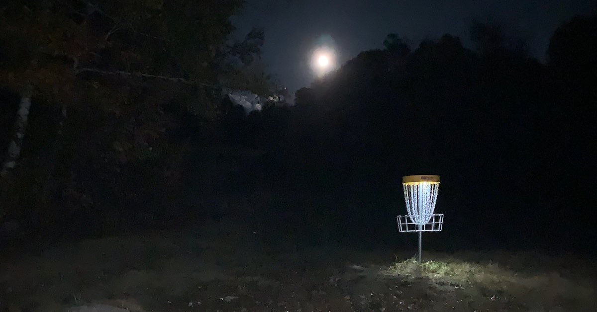 A full moon over a lit disc golf basket