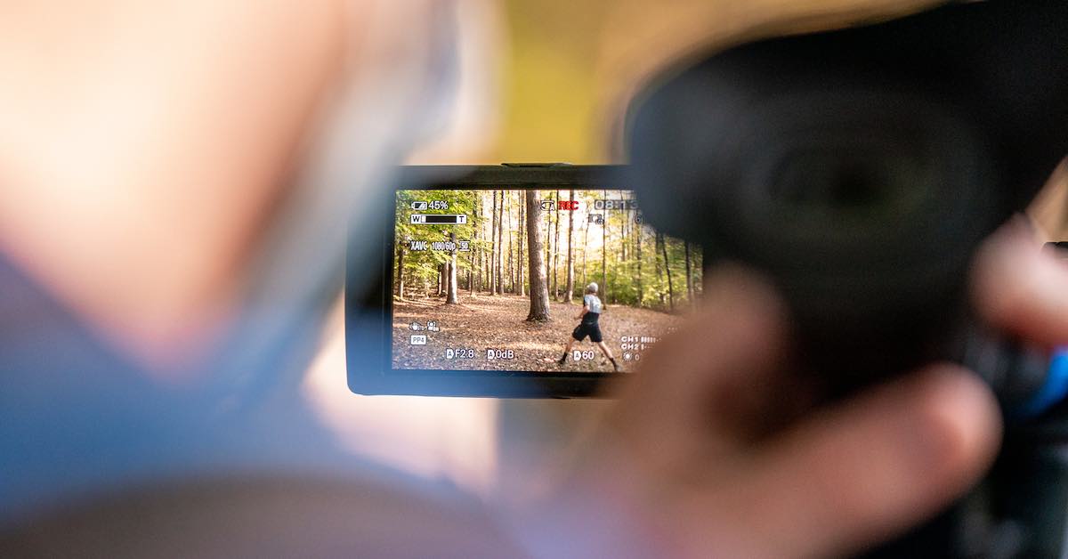 A blurry image of a camera operator surround a sharp image of a disc golfer being filmed as shown through the camera's display screen