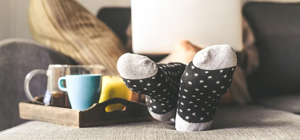 foot view of person wearing socks while sitting on a couch with laptop next to drink tray