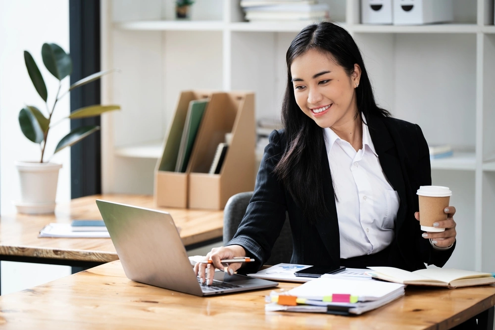 business woman holding a drink and working on her laptop
