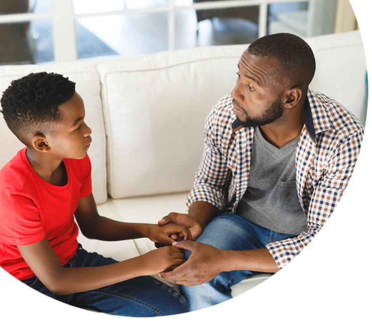 Serious african american father and son sitting on couch in living room talking and holding hands