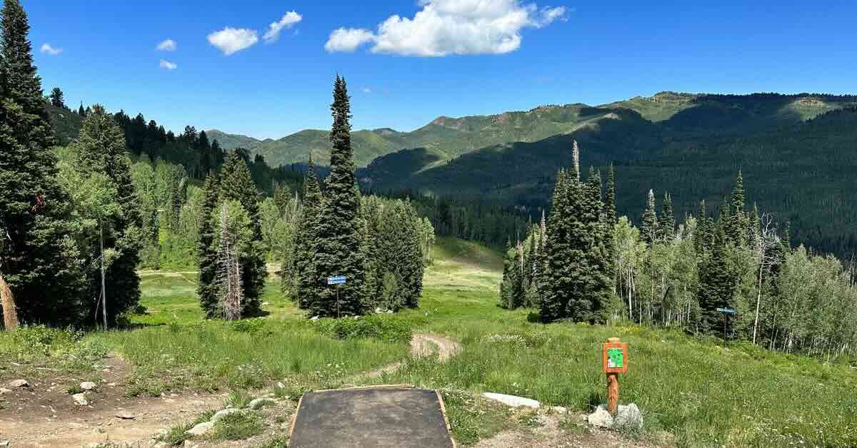 A disc golf basket tee looks to an expansive mountain view with many trees