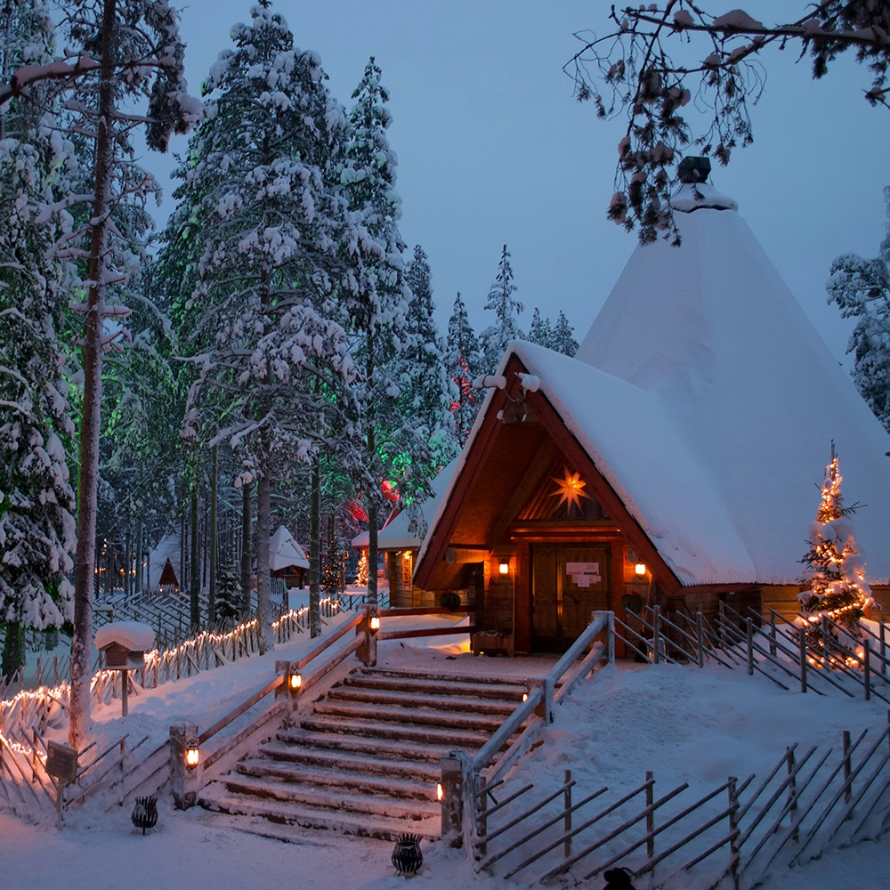 Cabin in the snowy woods of Rovaniemi, Finland lit up with Christmas lights.
