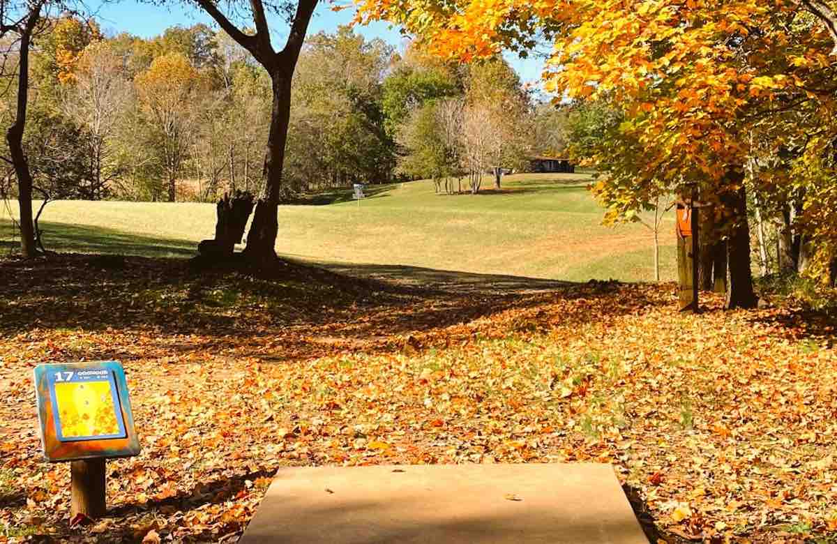 A concrete disc golf tee pad in a slightly wooded area leading to an open, mown fairway