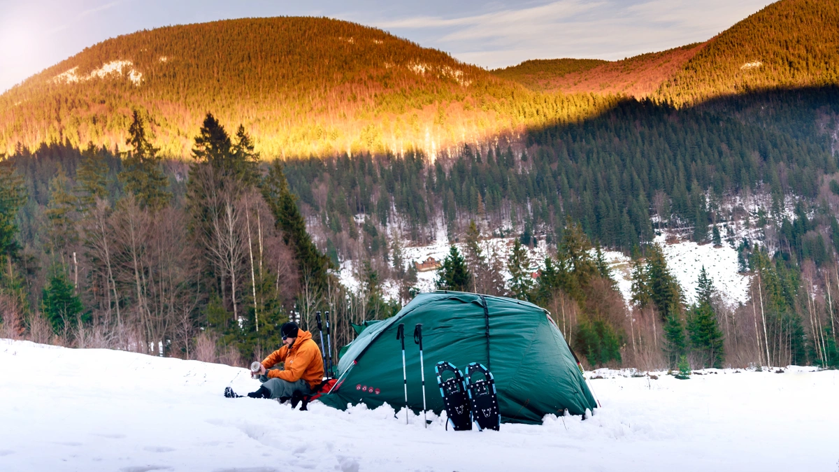 man with snowshoes and tent sitting in snow