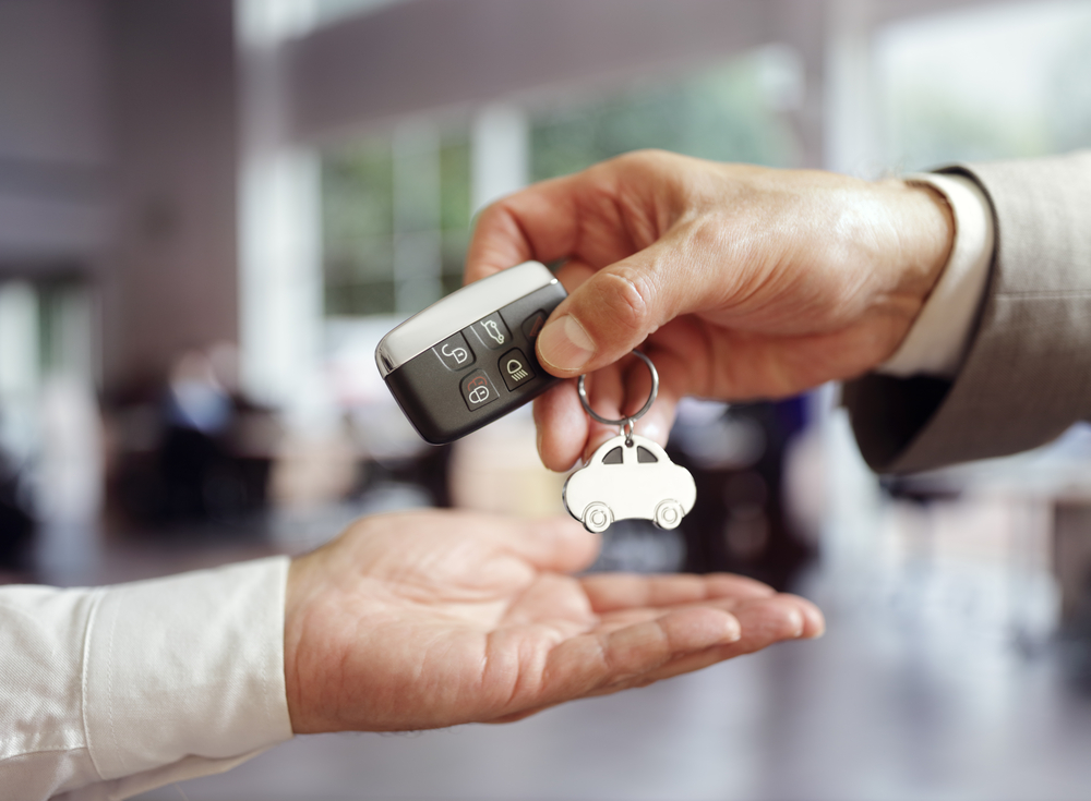 One person hands a car key to someone else. Only their hands and the car key fob are visible.