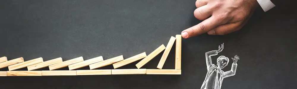 hand stopping dominoes from falling on stick figure