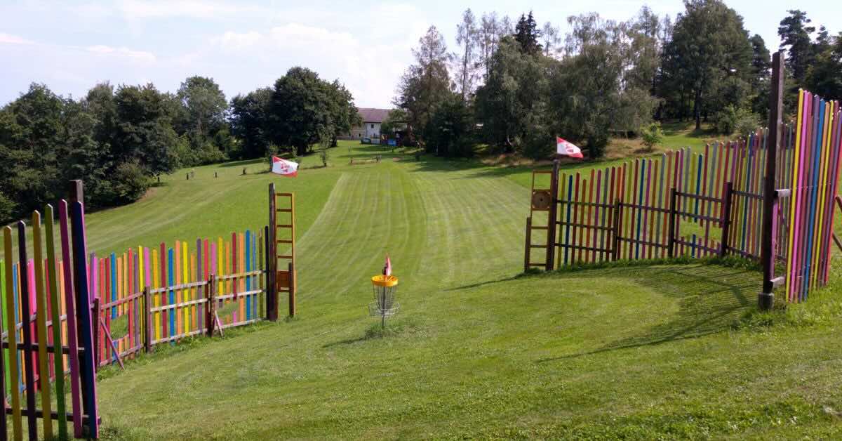 Disc golf basket in a well-mown area surrounded by a colorful fence