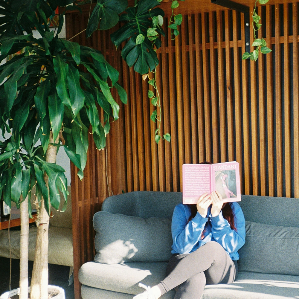 Woman reads on a grey couch with a book over her face.