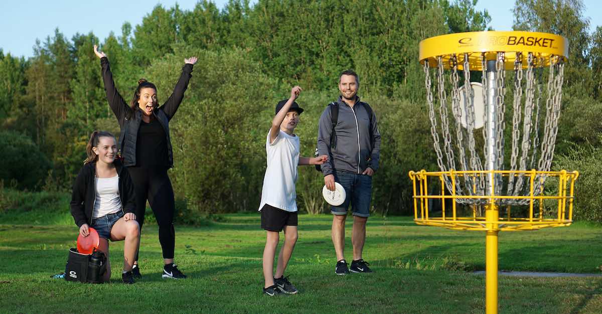 A family cheers as a boy's putt goes in a yellow disc golf basket