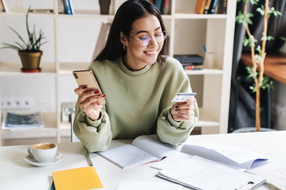 Woman looking at her credit card while holding her phone in her other hand