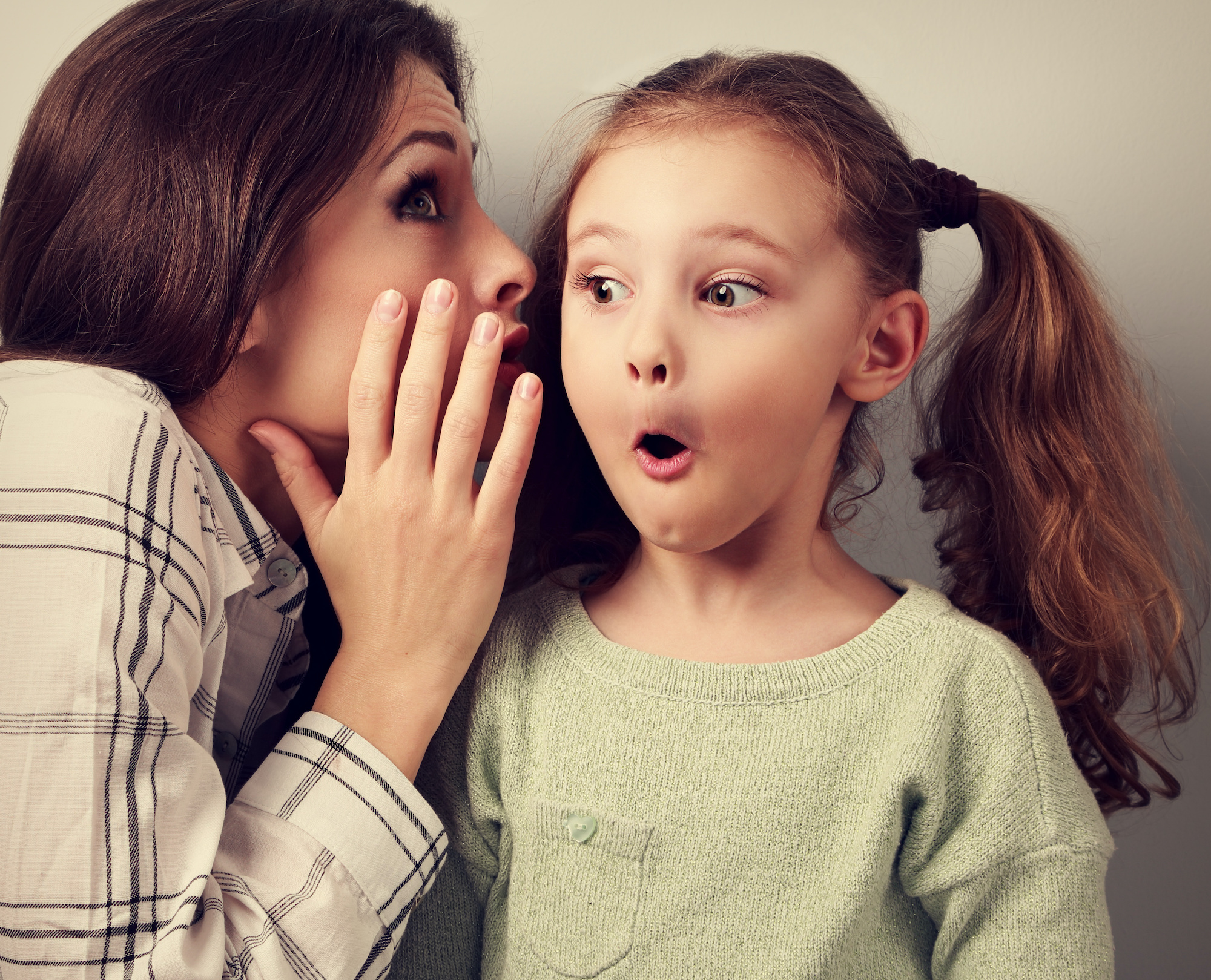 A young girl looks surprised as her mother whispers in her ear