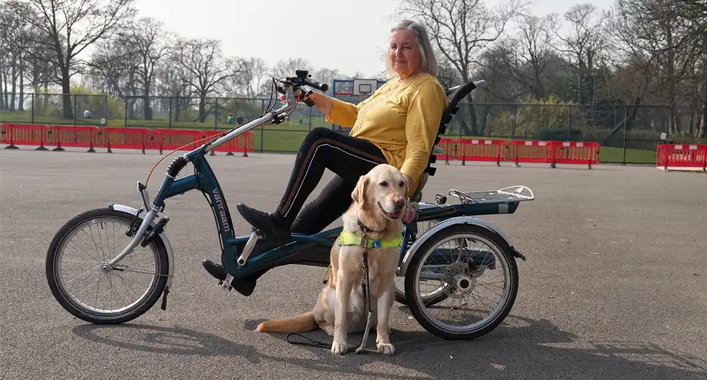 Woman rides adaptive bicycle with service dog.