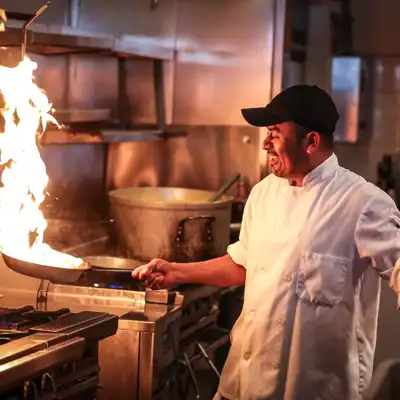 Chef sautes food with big flames coming off pan.