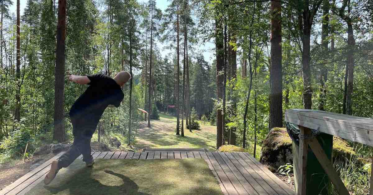 A man throws a forehand to a wooded fairway from a largen wooden platform with turf tee