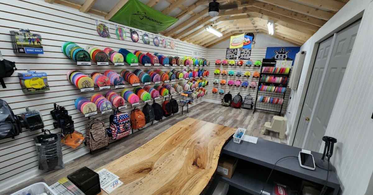 Interior of a small disc golf shop with racks of discs and bags n wall