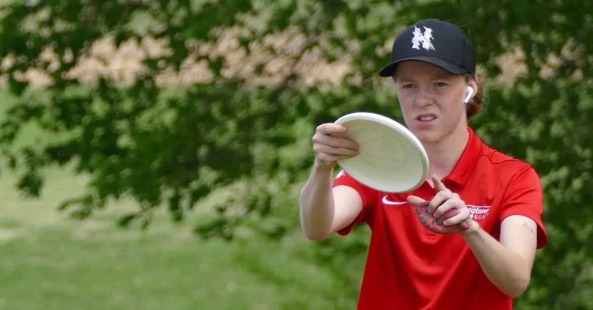 A woman in a red shirt lining up a putt with a disc golf putter
