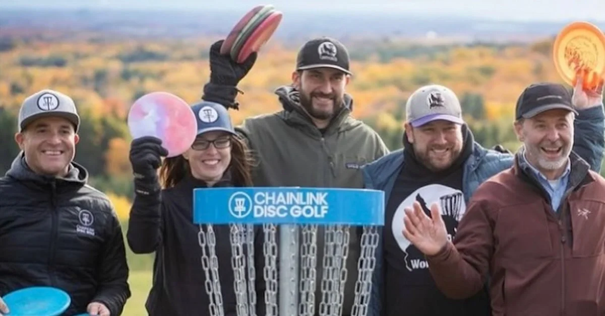 A group smiles with discs in front of a disc golf basket