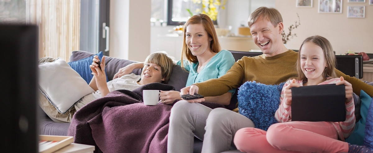 A family sat on a sofa streaming a movie on TV while using other devices.