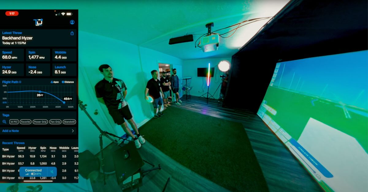 Young men in a big room with a projector and stats from a disc golf throw on the left